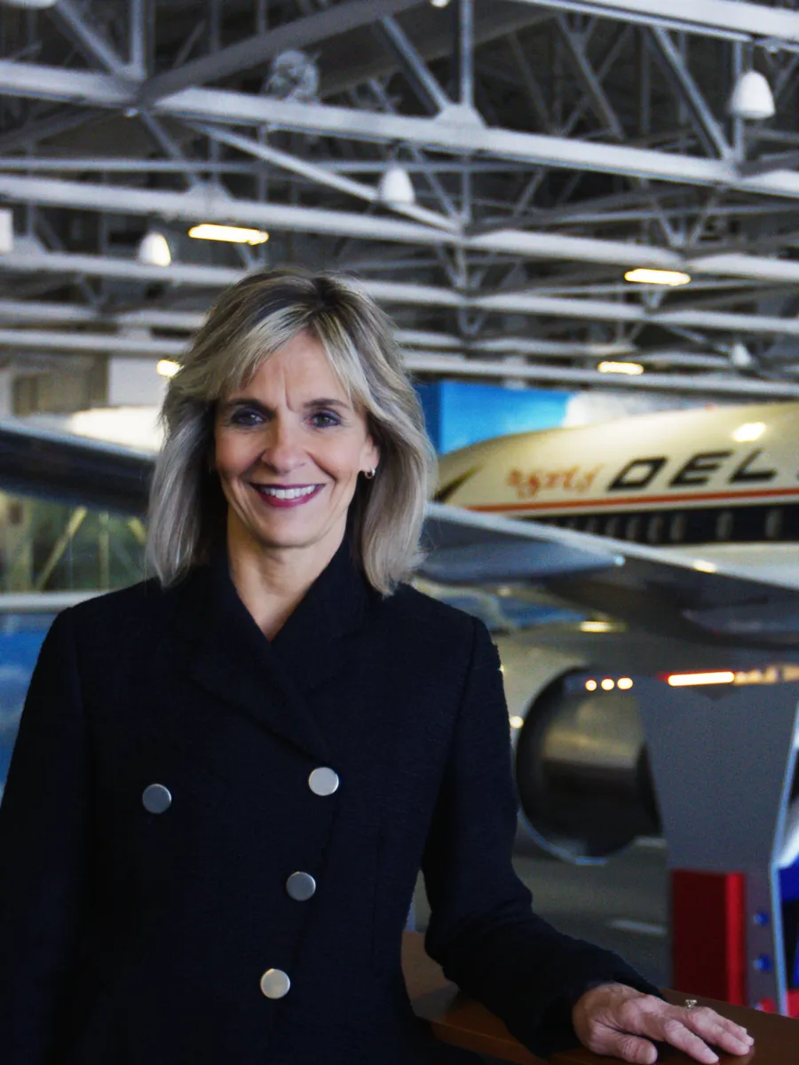 A close-up profile of Allison Ausband, the UGA Foundation Chair and Executive VP at Delta Airlines. She is in an airplane hangar and wearing a black coat.