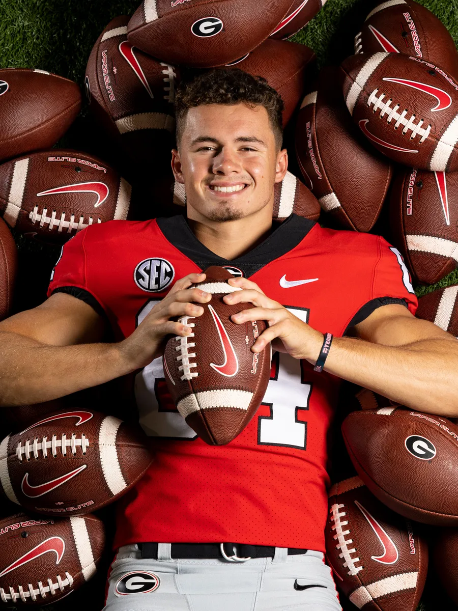 A profile photo of football player Ladd McConkey. He is wearing a University of Georgia football uniform for the Georgia Bulldawgs and laying on a pile of footballs.