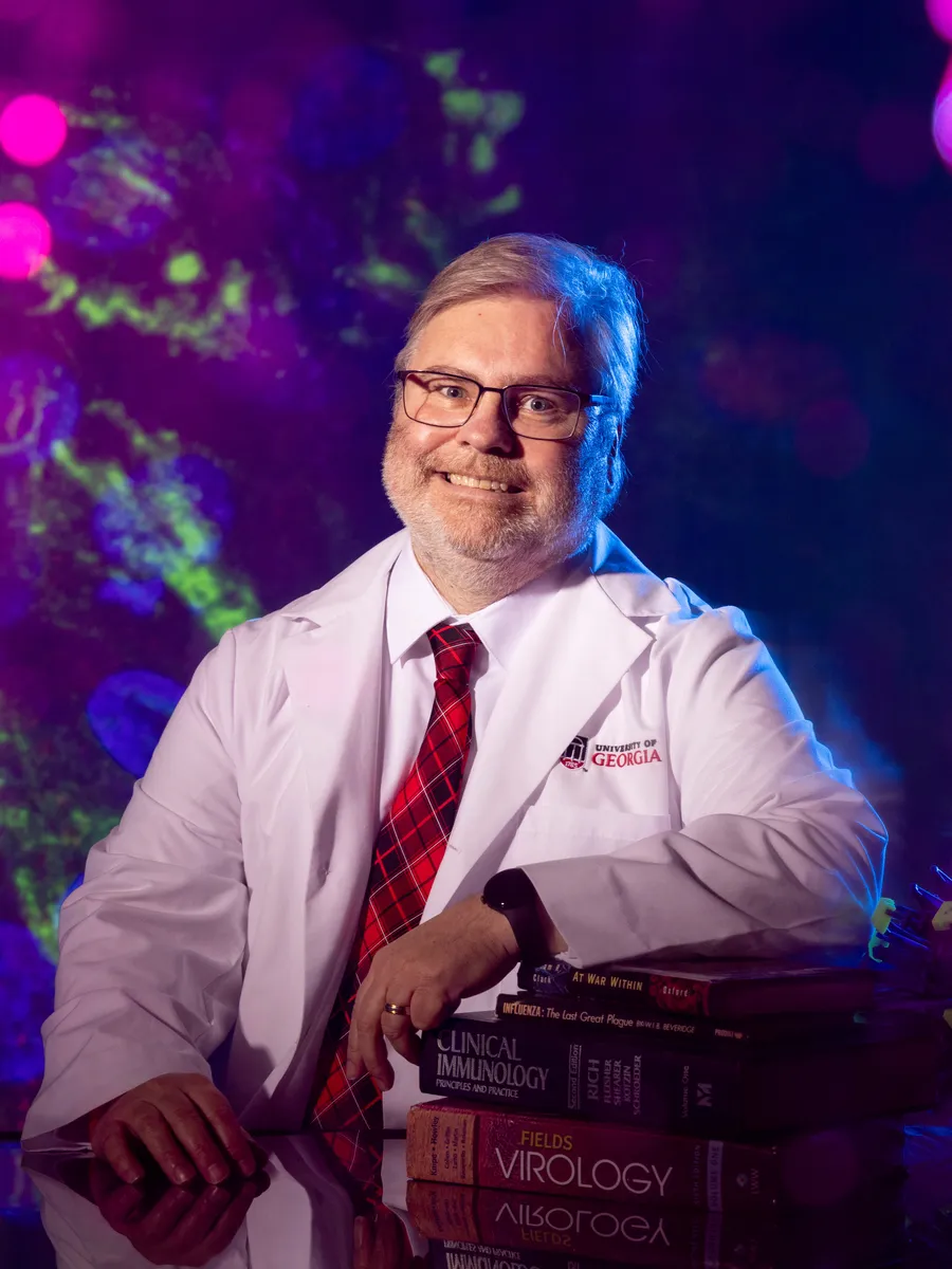 A profile photo of Mark Tompkins, a researcher at the University of Georgia. He is pictured in a white lab coat with the University logo.