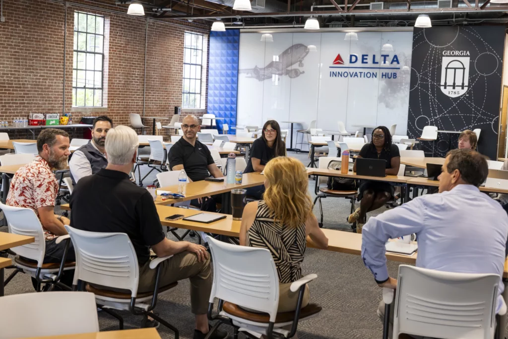 Attendees sit in a circle of chairs talking at the Delta Innovation Hub, with UGA branding on the wall