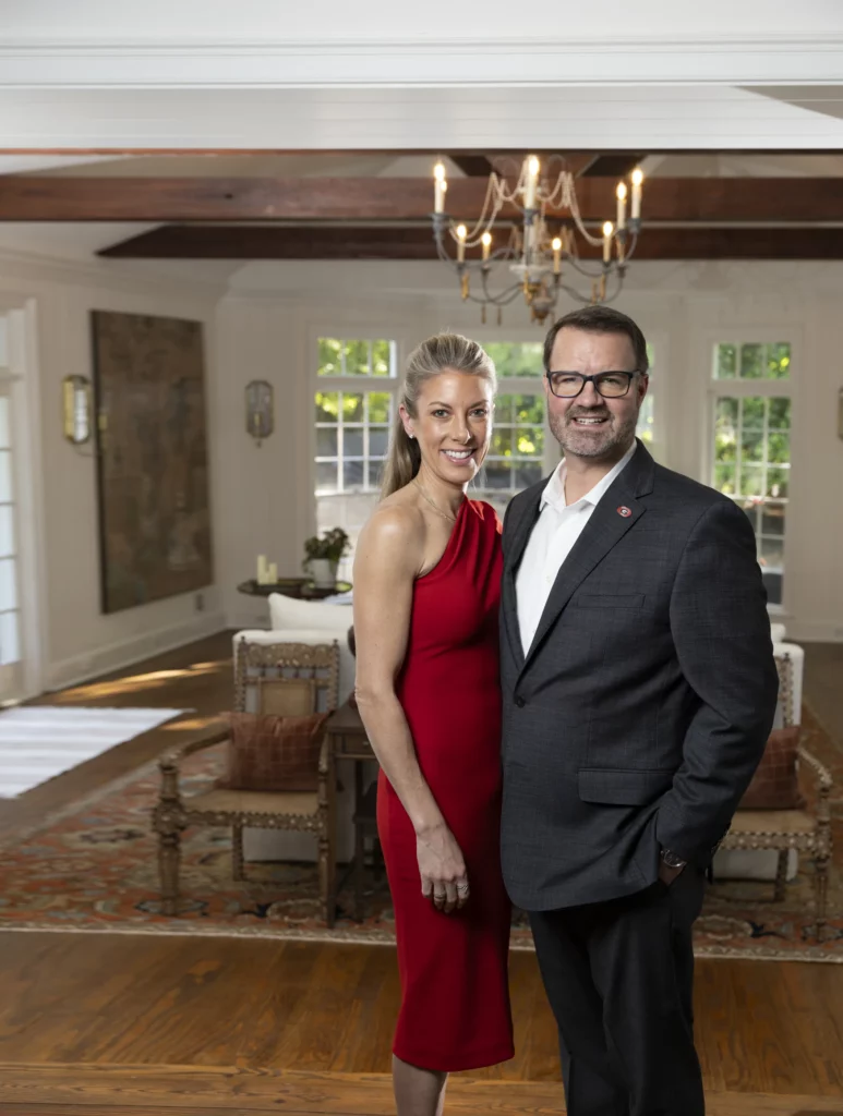 Carrie and Paton Faletti stand together in a living room beneath a candle chandelier