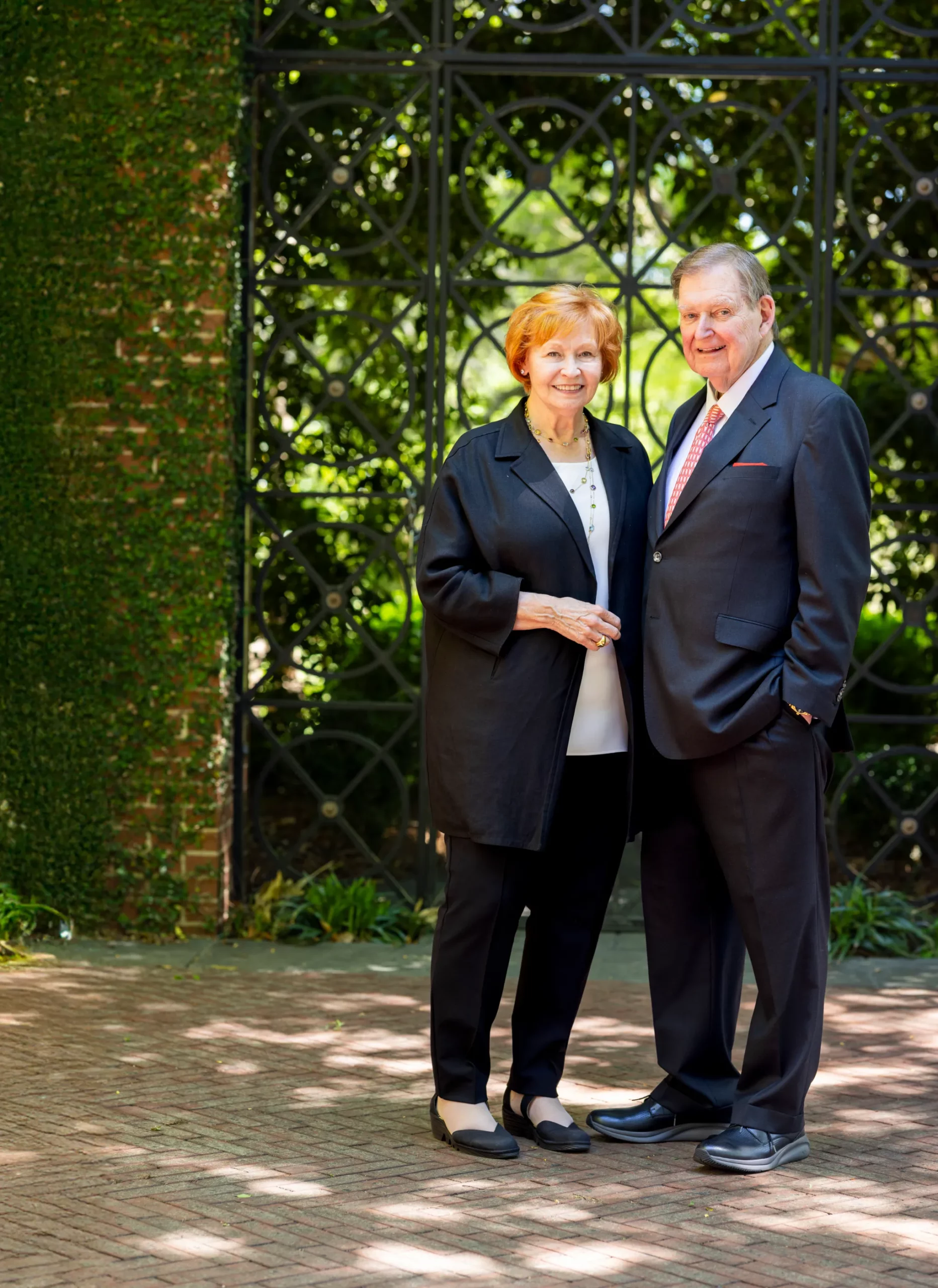 Doug and Kay Ivester stand together on a brick courtyard in front of an ornate iron gate