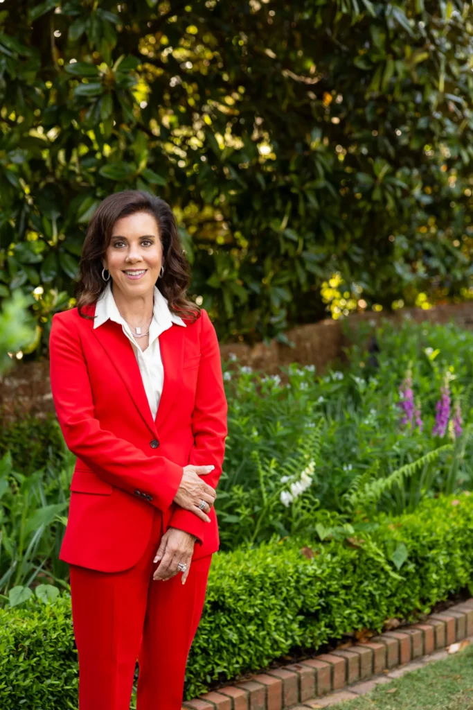 Elizabeth Correll Richards, in a red suit, stands in a garden in front of a magnolia tree